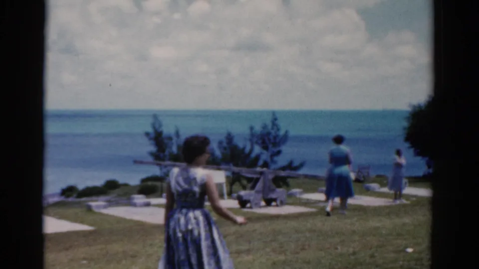 A handheld 8mm view shows visitors near a coastal lawn and walkway, with the ocean and cloudy sky beyond.
