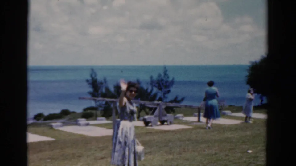 1975 Florida 8mm frame of a woman waving toward the camera as other women stand near paths above the ocean.