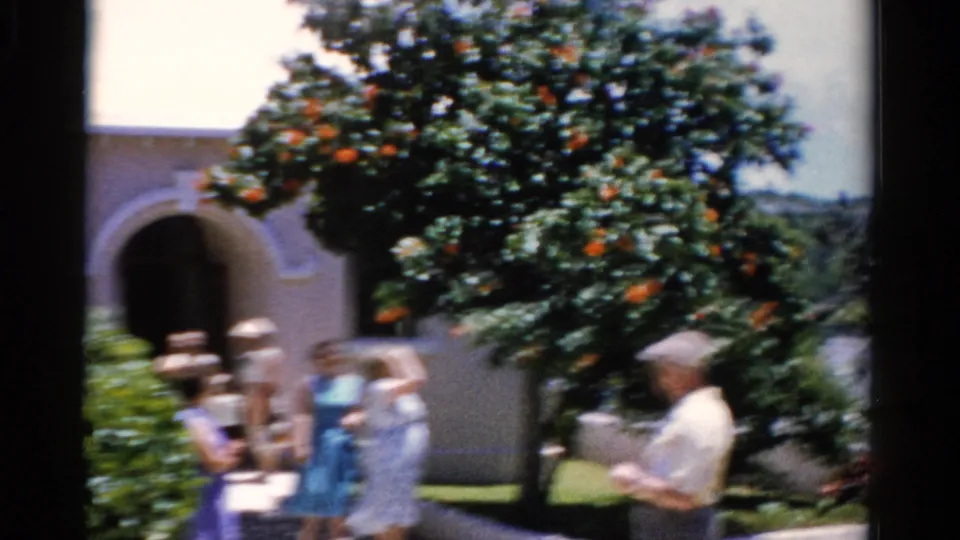 1975 Florida 8mm frame with adults in summer clothing near an arched building entrance and orange-like fruit tree.