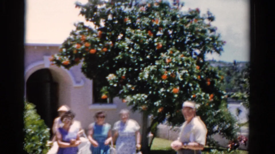 Older adults appear outside a Florida church-like stucco building in 1975, framed by a fruiting orange tree.