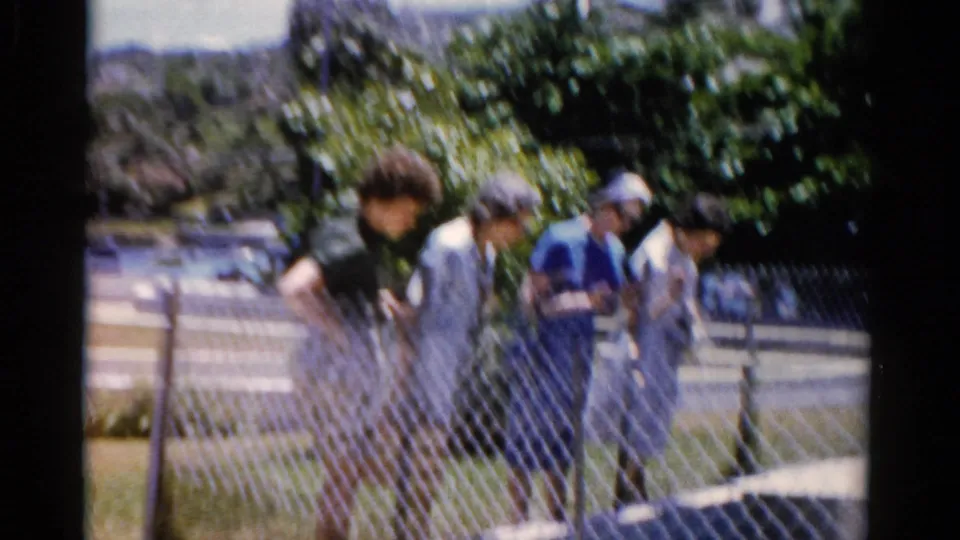 The group continues along a sunny Florida sidewalk in 1975, seen through soft 8mm focus and frame-edge vignetting.
