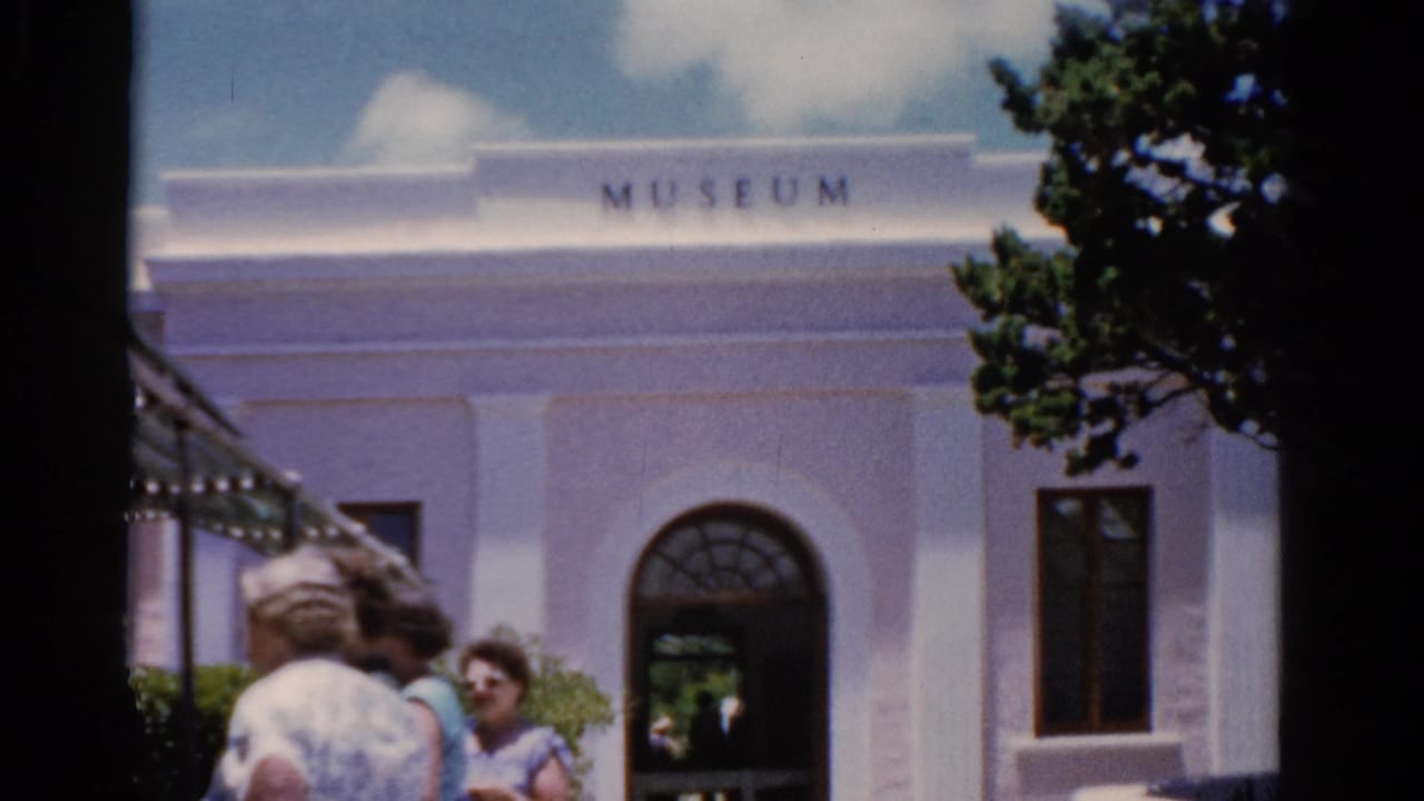 A white building with museum lettering and visitors near an arched doorway.