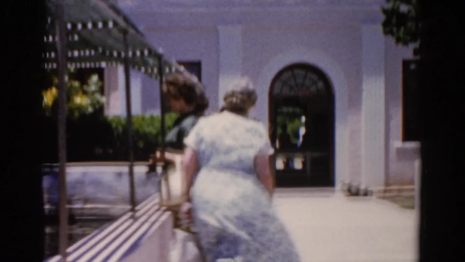 Two women in summer clothing walk toward an arched museum entrance in Florida home-movie footage from 1975.