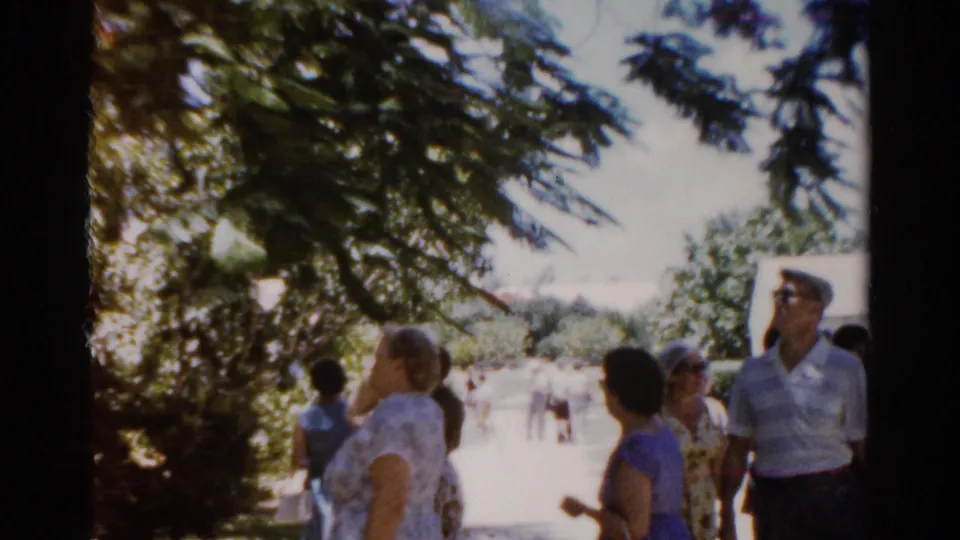 Florida 1975 frame with adults in summer clothing under tree branches, including women in dresses and a man wearing sunglasses.
