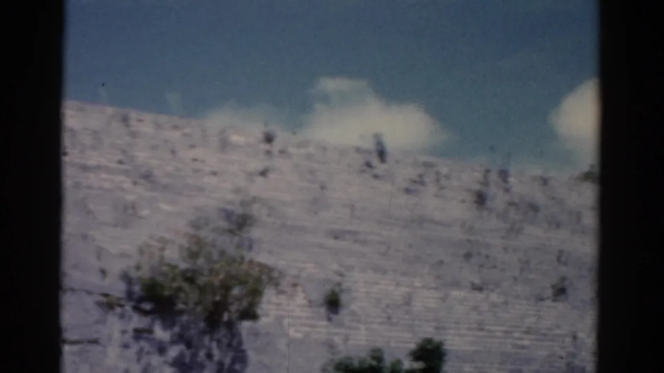 1975 Florida 8mm view across a pale rocky hillside with scattered shrubs, blue sky, and white clouds.