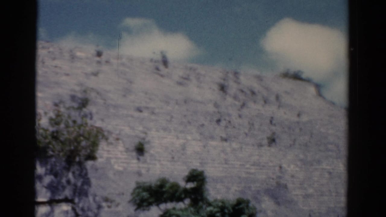 Large stepped gray stone structure under a blue sky with clouds and dark film borders.