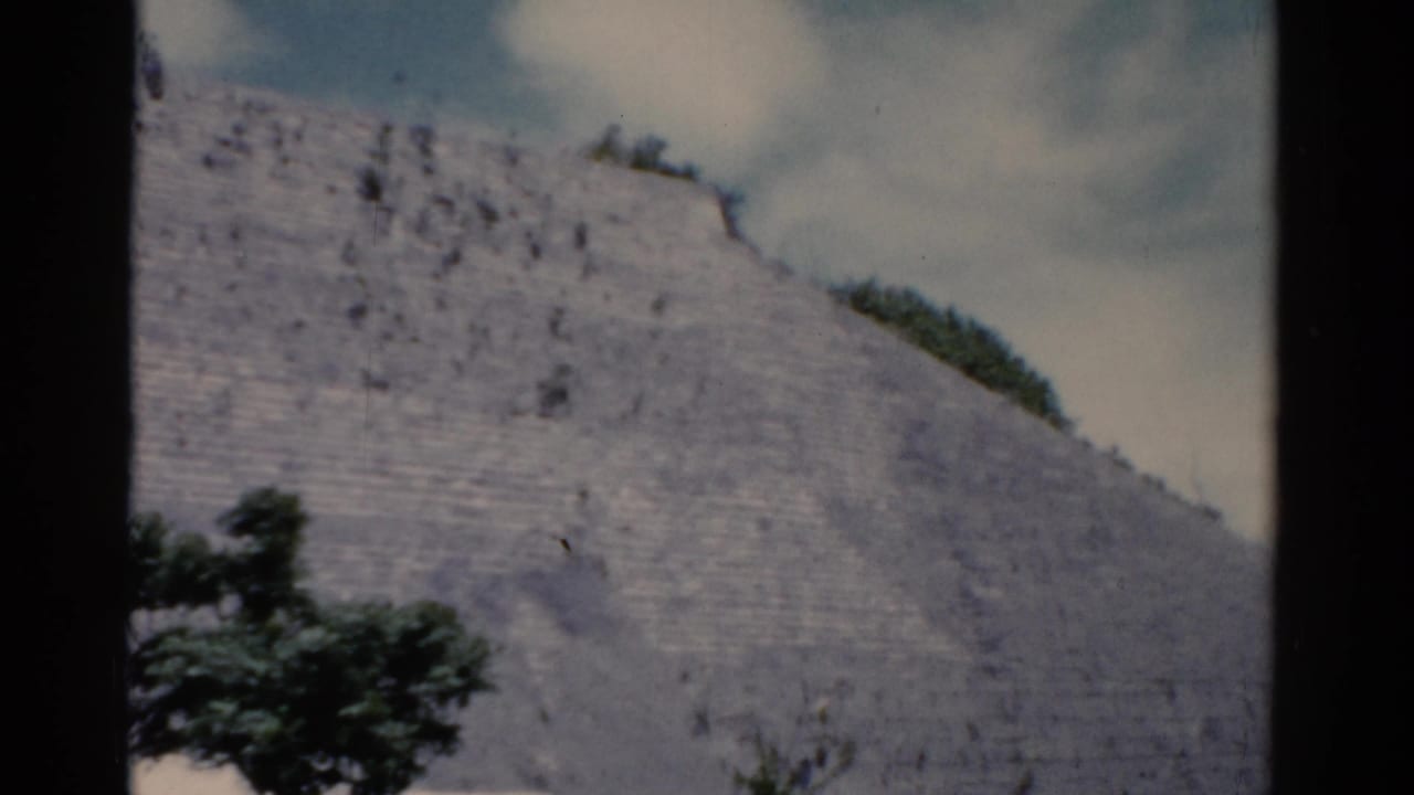 1975 8mm frame of a weathered stepped stone surface with sparse trees and a bright clouded sky, location listed as Florida.