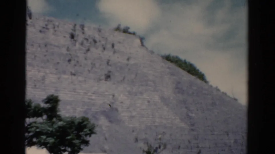 1975 8mm frame of a weathered stepped stone surface with sparse trees and a bright clouded sky, location listed as Florida.