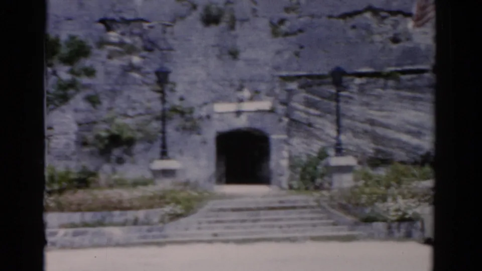 1975 Florida frame centered on a stone entrance with steps, lampposts, landscaped beds, and a dark arched doorway.