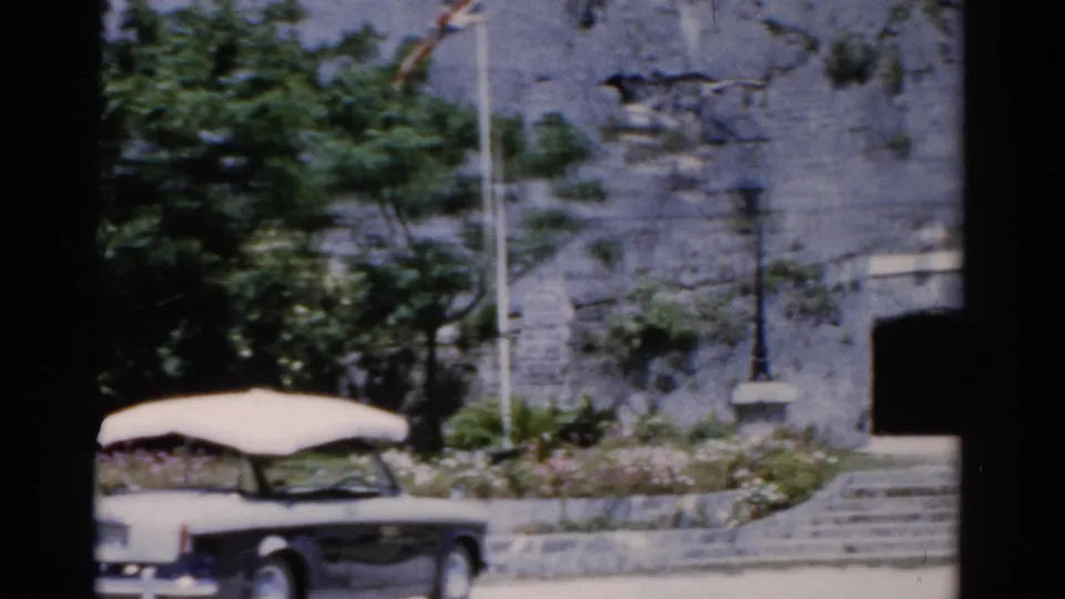 1975 Florida 8mm frame showing the rear of a white convertible near stone steps, greenery, and a dark entrance.