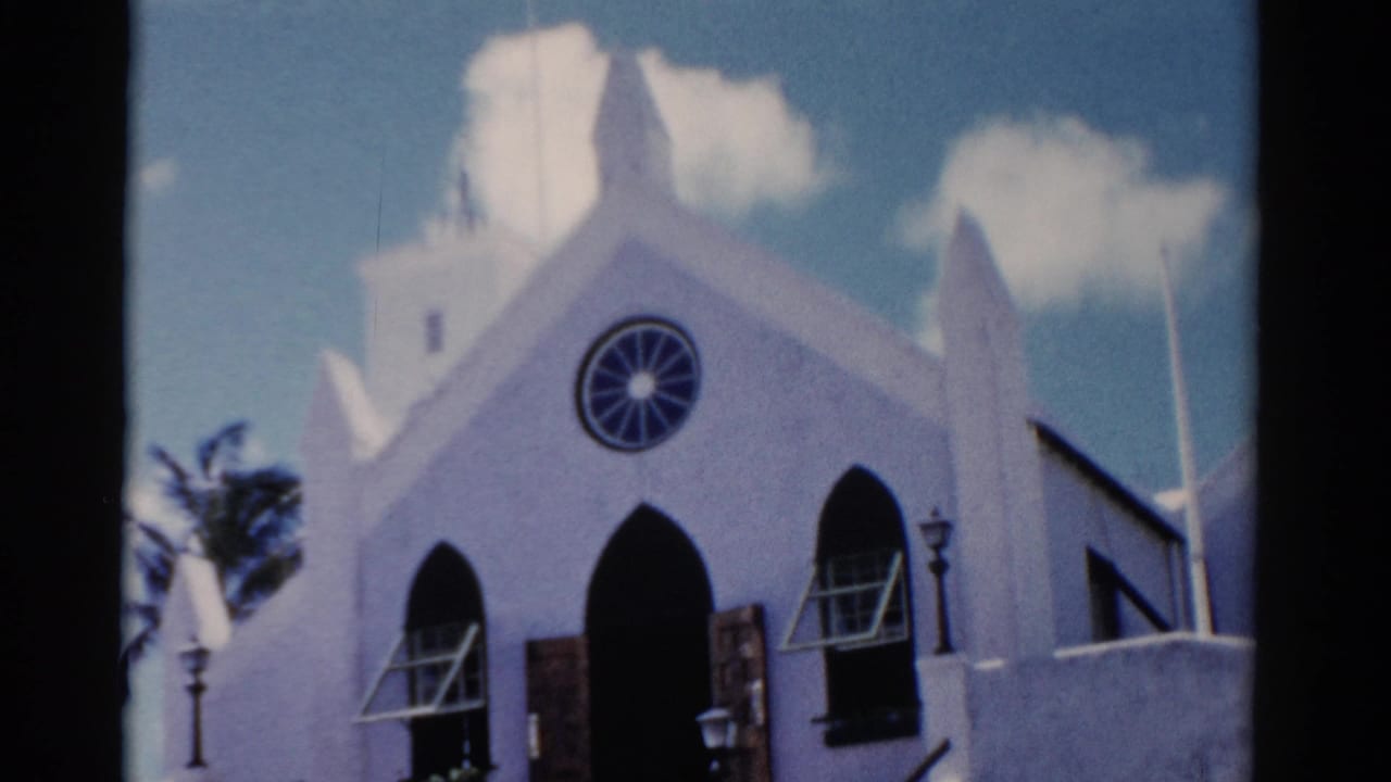 1975 Florida 8mm frame showing a white church facade with pointed arches, a circular rose window, lampposts, and palm foliage.