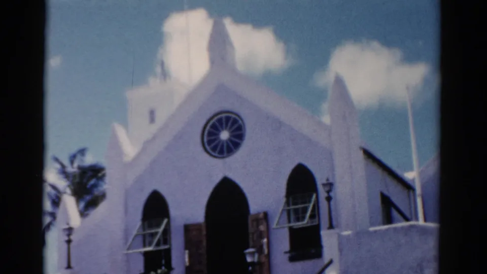 1975 Florida 8mm frame showing a white church facade with pointed arches, a circular rose window, lampposts, and palm foliage.