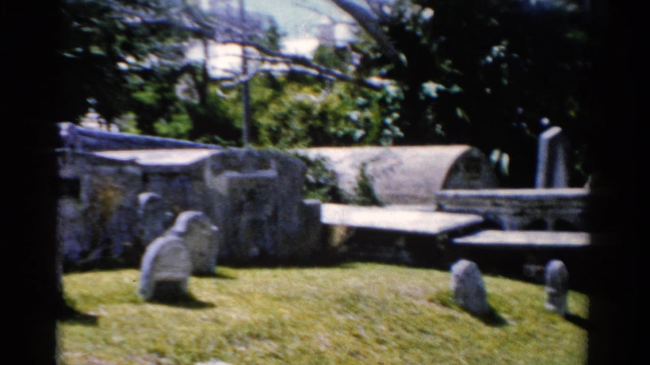 Florida 1975 cemetery view with weathered stone tombs, rounded grave markers, lawn, and trees in soft 8mm focus.
