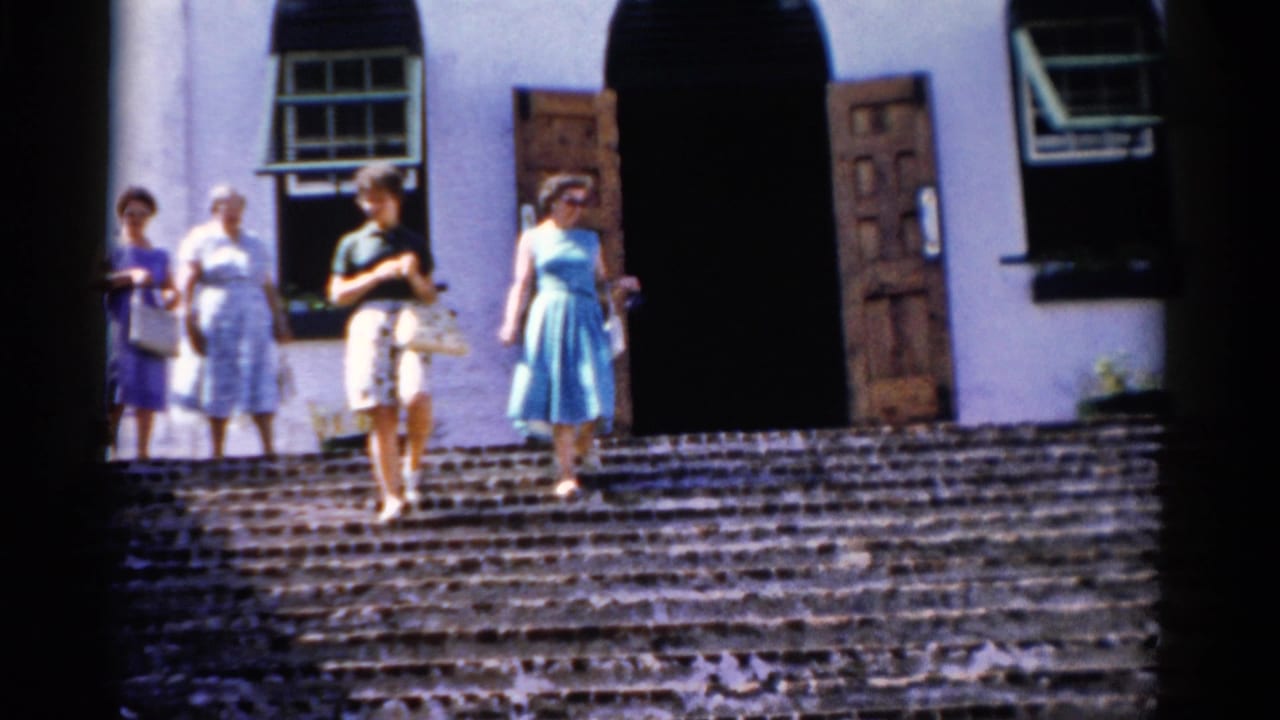 1975 Florida 8mm frame showing women in dresses and handbags on broad steps outside a white building with dark doorways.