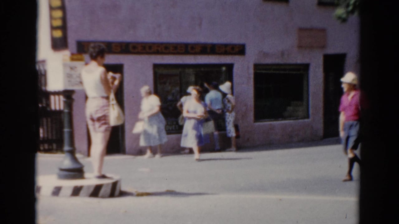 1975 Florida street frame with a woman on the divider, pedestrians by the signed gift shop, and a man in a white hat at the edge of view.