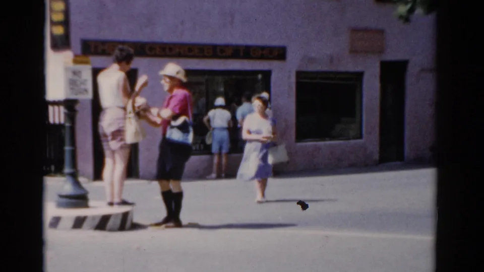1975 Florida street frame where the man in a pink shirt appears to meet the woman on the divider, with pedestrians and shop signage behind them.