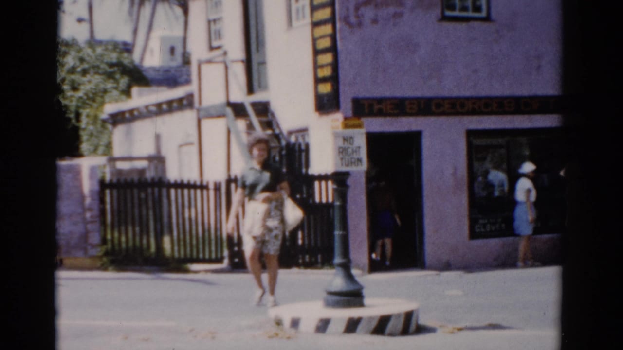 1975 Florida frame of a woman in a green shirt and patterned skirt walking past The St Georges Gift Shop entrance and street sign.