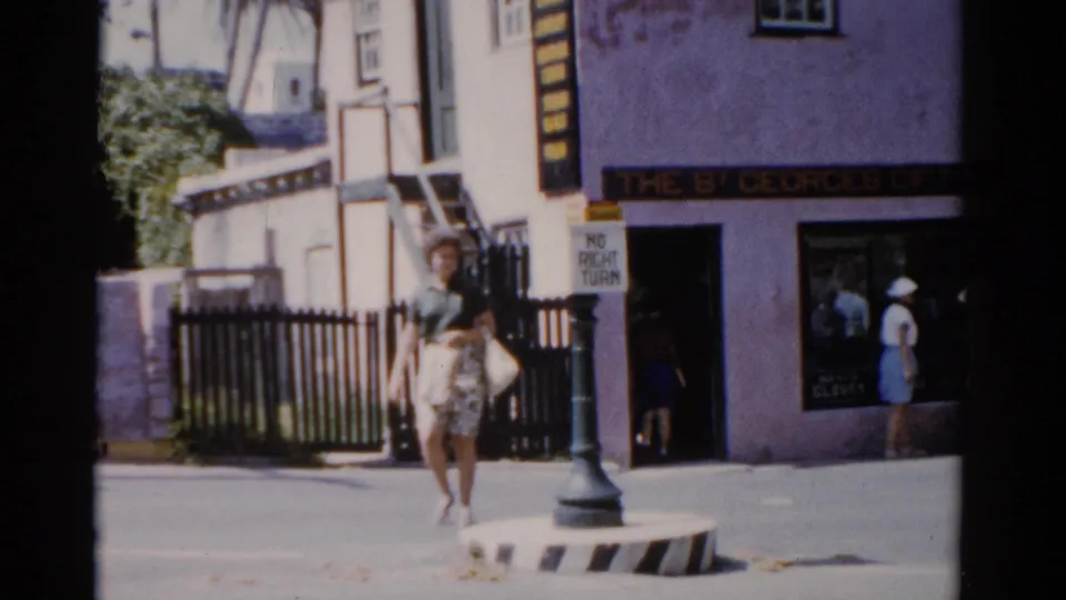 1975 Florida frame of a woman in a green shirt and patterned skirt walking past The St Georges Gift Shop entrance and street sign.