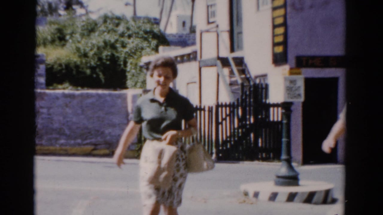 Woman in a green top walks near a pastel building and black fence.