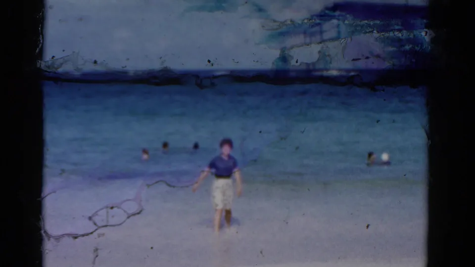 A woman stands at the shoreline in 1975 Florida footage while swimmers are scattered in turquoise ocean water behind her.