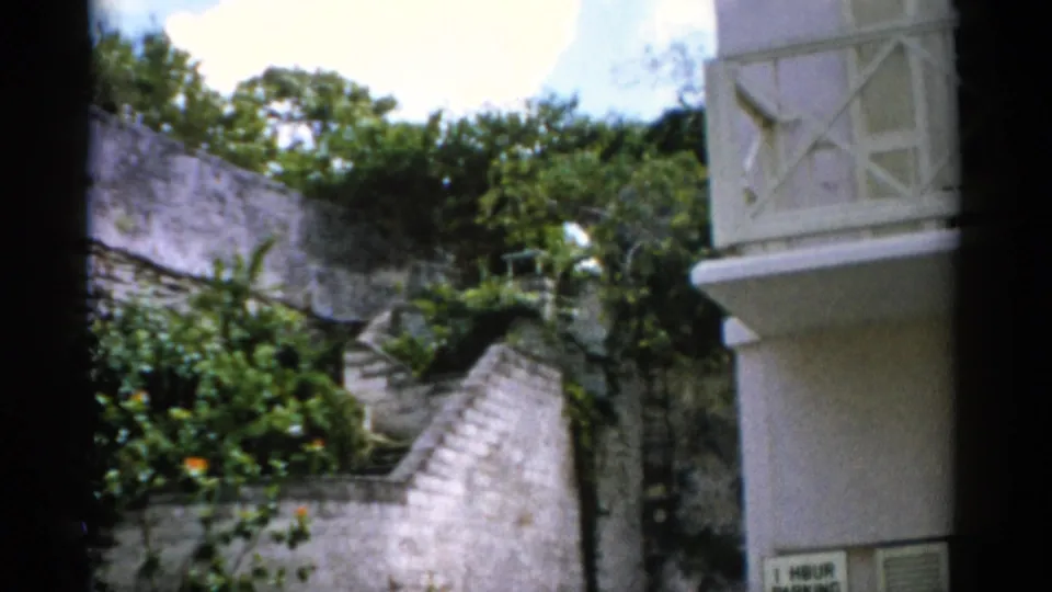 1975 Florida 8mm frame showing a stone staircase rising through greenery beside a white building with a decorative balcony.