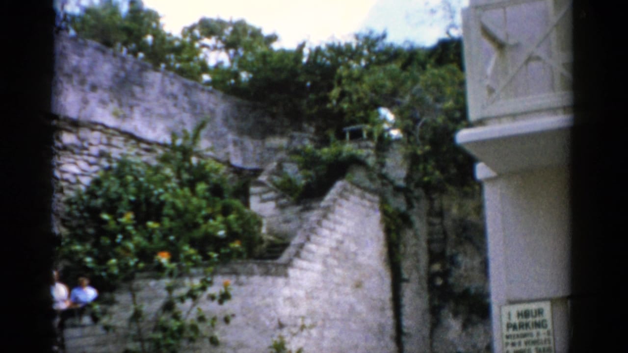 Two adults stand beside a stone stairway in a lush walled garden.