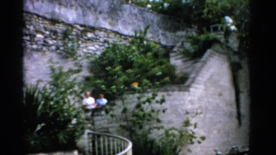 The couple appears on a curved stair landing in a landscaped Florida garden, framed by stone walls and white railing.