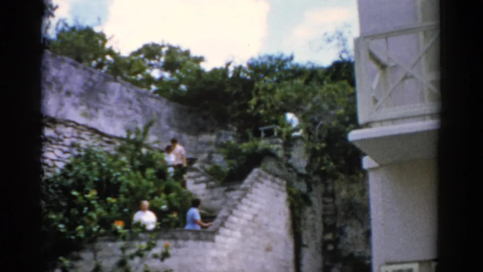 1975 Florida 8mm frame with adults walking and standing on a winding stone staircase in a planted outdoor garden area.