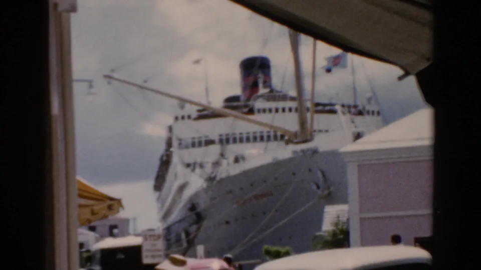 1975 Florida harbor view of a large white cruise ship seen from a shaded window or structure, with awning and parked cars below.