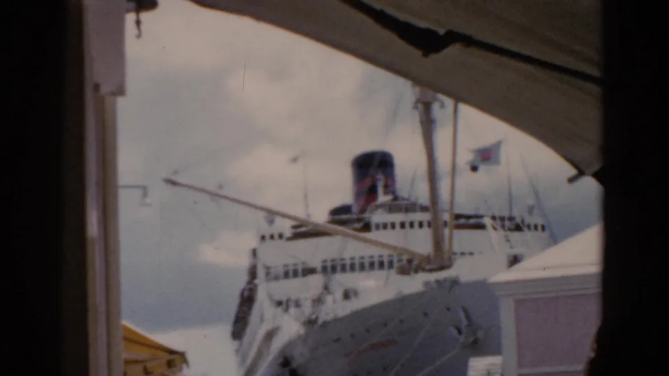 1975 Florida home-movie frame showing a large white cruise ship and smokestack viewed through a window or deck opening.