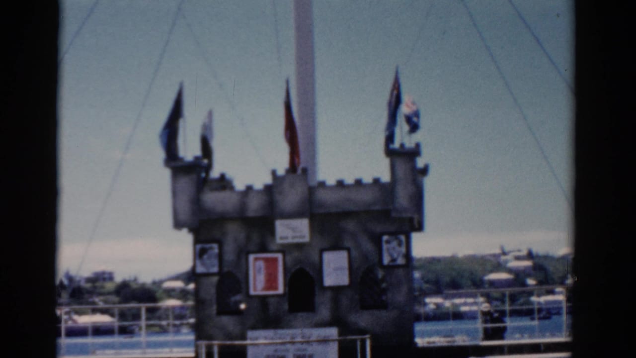 Castle-like dockside structure with flags and signs beside a waterfront railing.