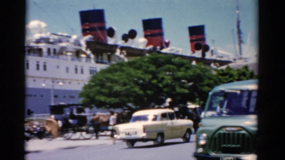 1975 Florida waterfront traffic frame showing a green van, pale station wagon, carriages, pedestrians, and a docked passenger ship.