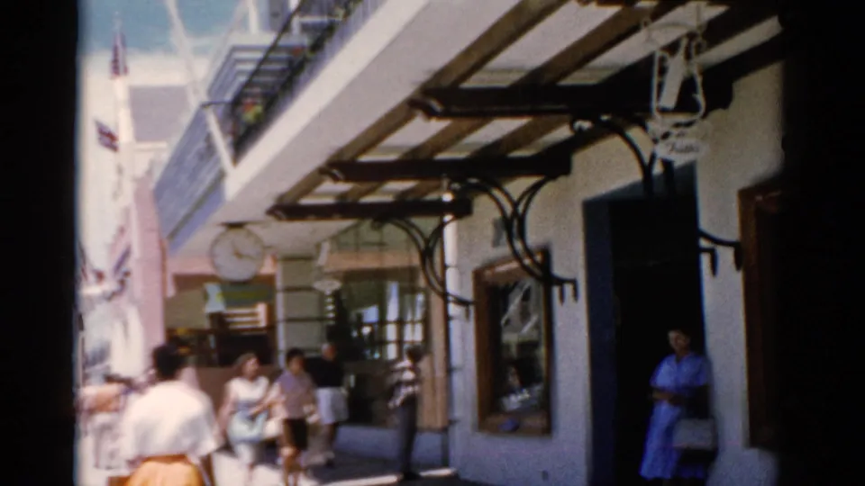 1975 Florida street view with shoppers on a commercial walkway, a clock sign, and a woman in a blue dress by the entrance.