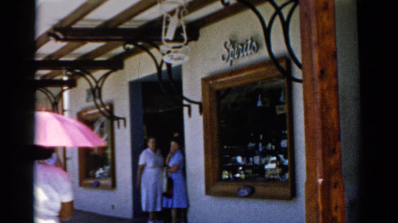 Reported Florida 1975 street frame showing two women near a storefront while a pink umbrella moves through the foreground.