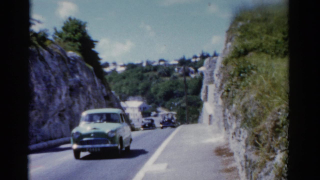 Light green car driving toward the camera on a narrow road between rocky slopes.
