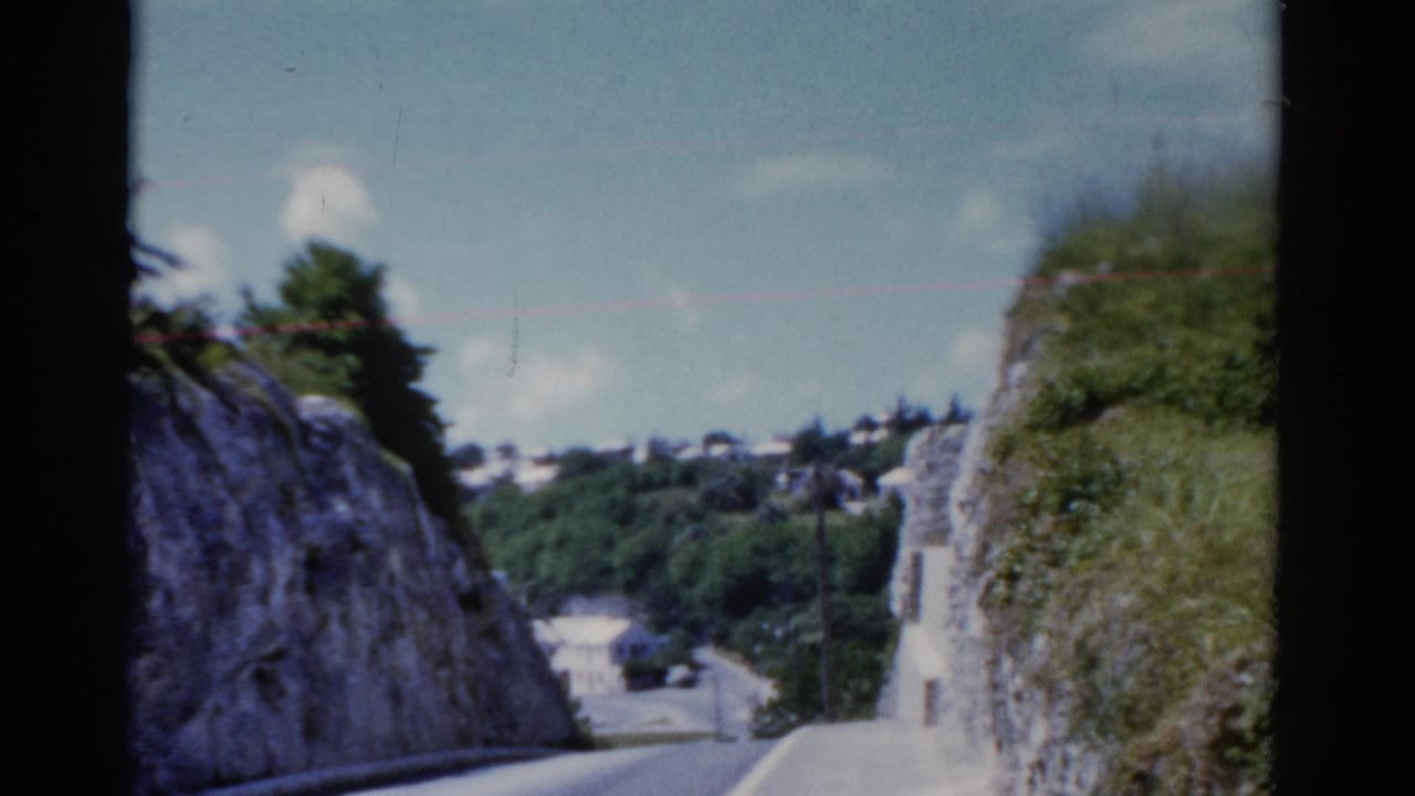 1975 8mm home-movie view of a narrow road passing between rocky slopes and green vegetation, location noted as Florida in metadata.