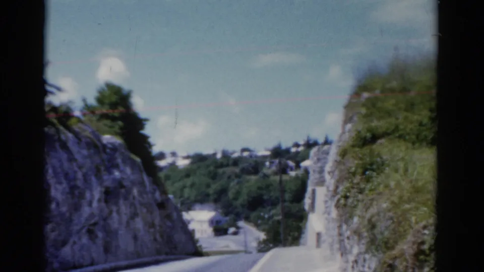 1975 8mm home-movie view of a narrow road passing between rocky slopes and green vegetation, location noted as Florida in metadata.