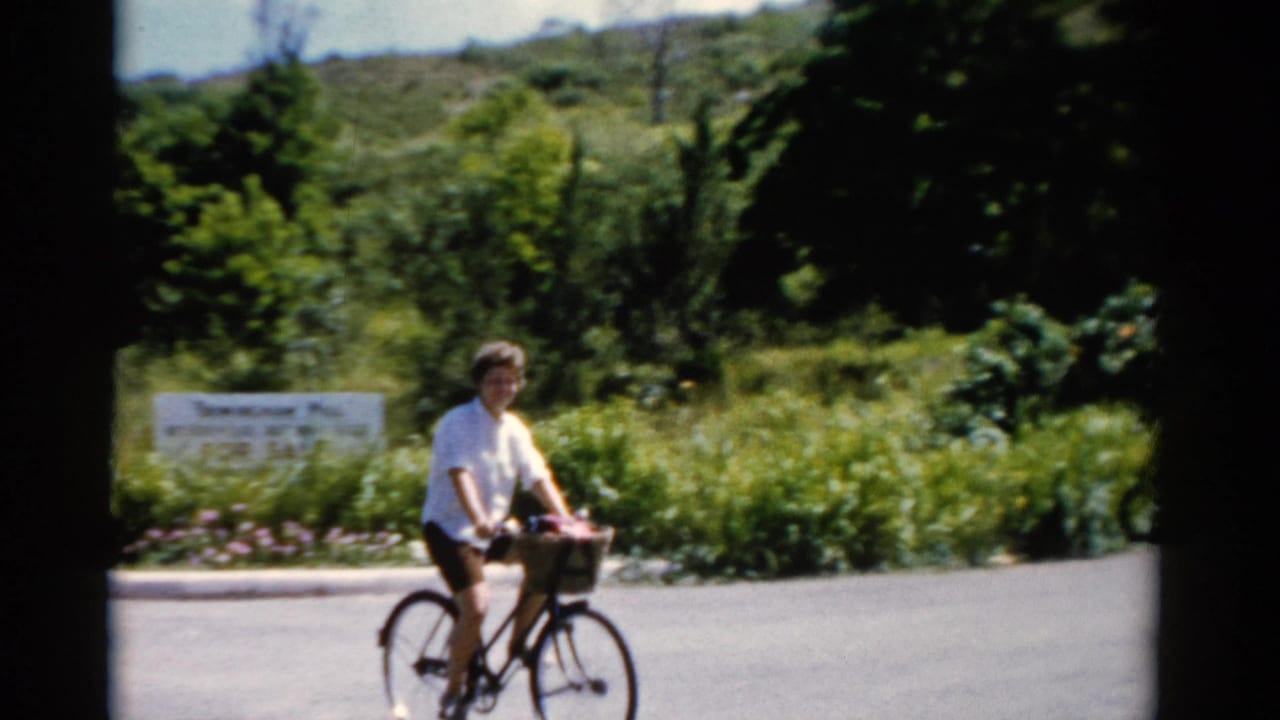 Woman on a bicycle moves along a paved road with greenery behind her.