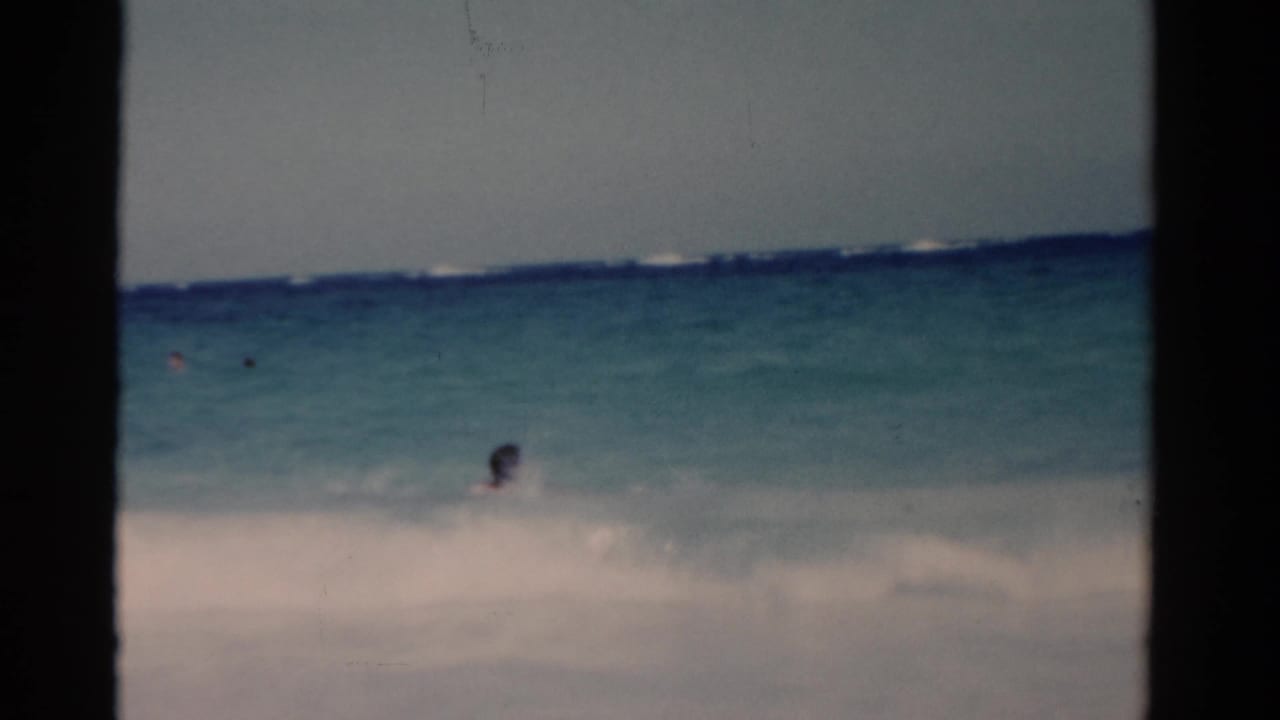 1975 Florida 8mm beach footage showing white sand, blue-green water, and small distant swimmers in the surf.