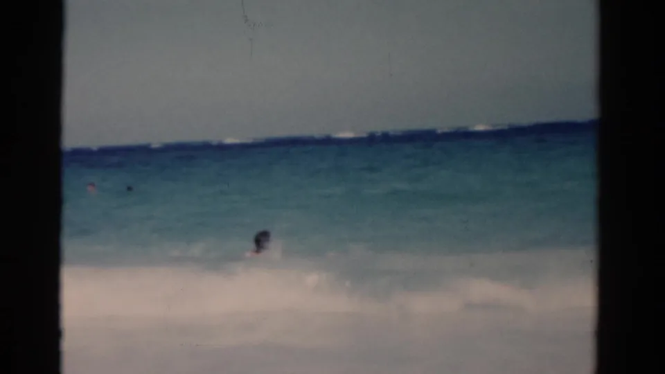 1975 Florida 8mm beach footage showing white sand, blue-green water, and small distant swimmers in the surf.