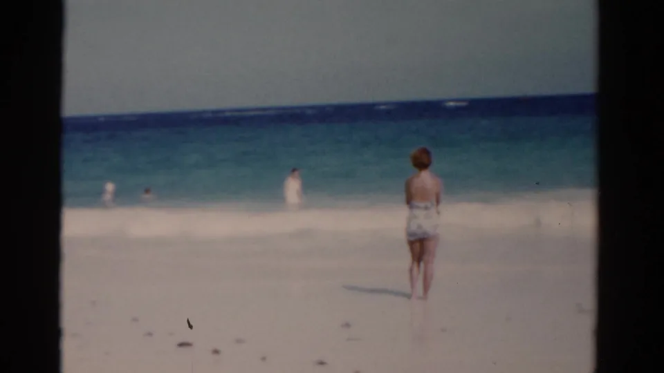 Soft 8mm beach view from Florida in 1975 with a woman standing alone in the foreground and swimmers beyond her in the surf.