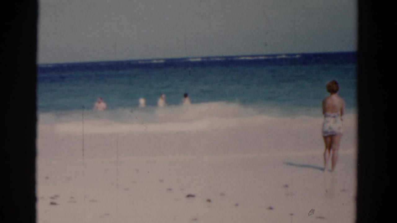 1975 Florida beach footage frame with the woman near the right edge and small figures visible in the shallow waves.