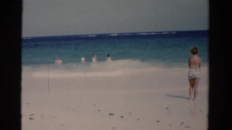 1975 Florida beach footage frame with the woman near the right edge and small figures visible in the shallow waves.