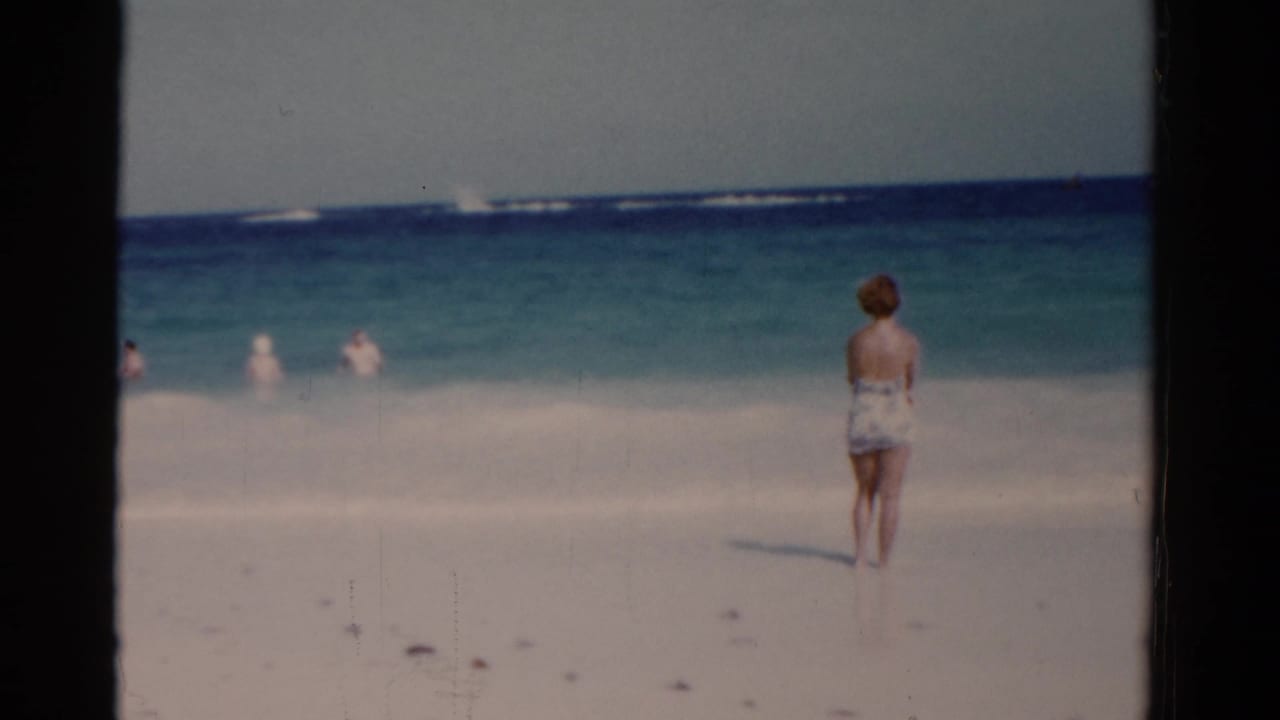 The woman remains near the Florida shoreline, facing the blue-green water and distant swimmers in this 8mm beach frame.