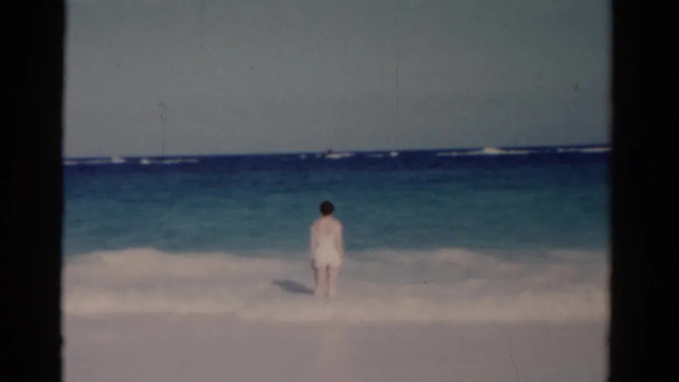 A distant figure faces the ocean from the shallow surf in a soft 1975 Florida 8mm beach frame.