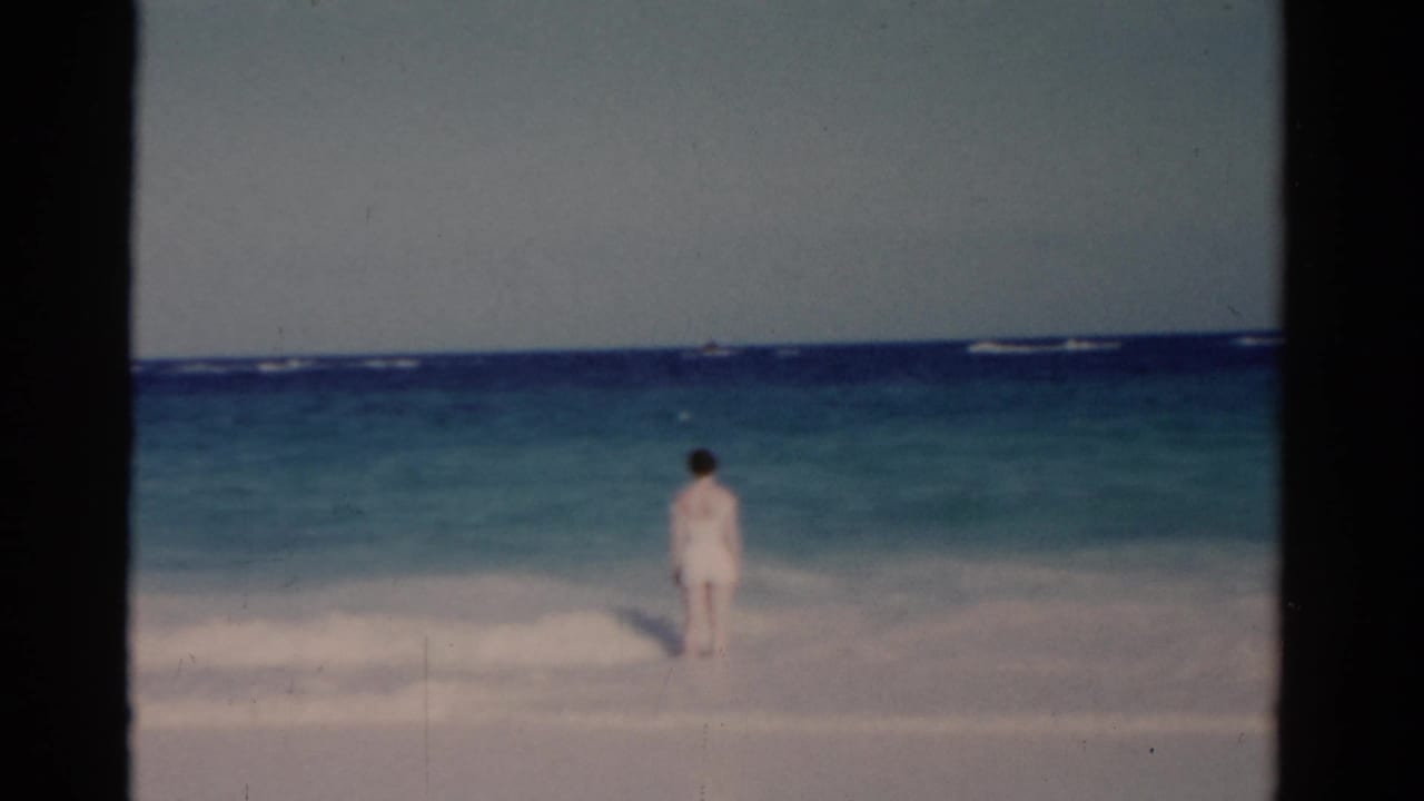 Woman standing in ocean surf with waves breaking behind her.
