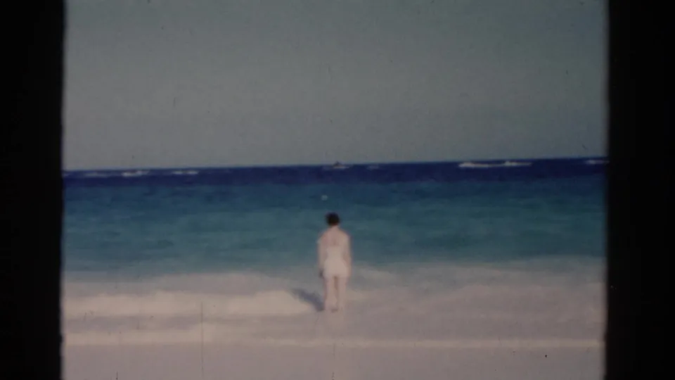 The woman remains in the Florida surf, framed at a distance against turquoise water and low white waves.