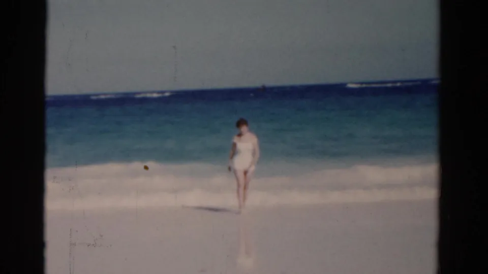 At the end of the 1975 Florida beach clip, the woman approaches the wet sand as waves break behind her.