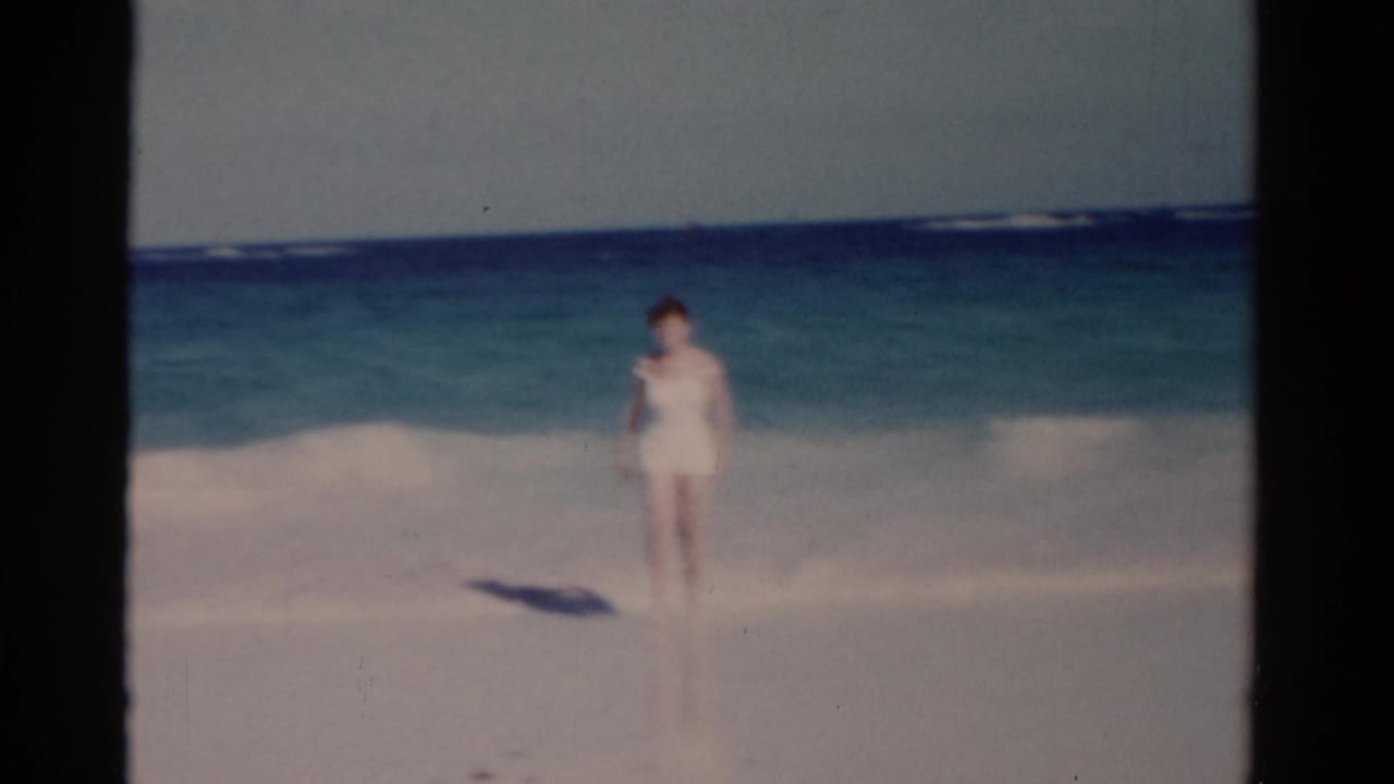 Woman walking along a bright beach with waves breaking behind her.