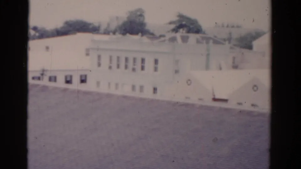 1975 Florida 8mm frame showing light-colored buildings, rooflines, windows, and dark trees beyond the structures.